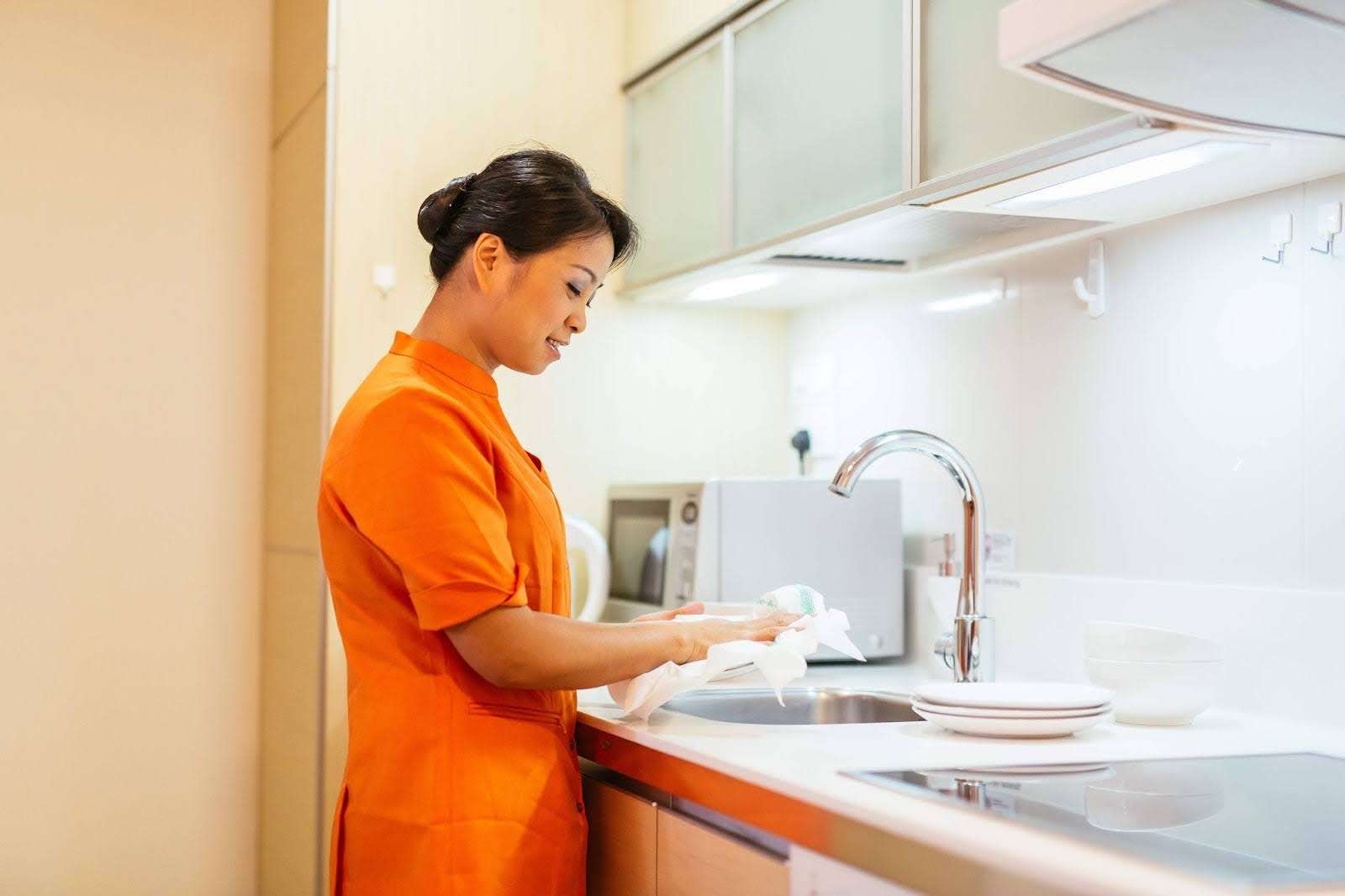 Housekeeping staff washing a plate in a modern, fully equipped kitchen of a luxury serviced apartment