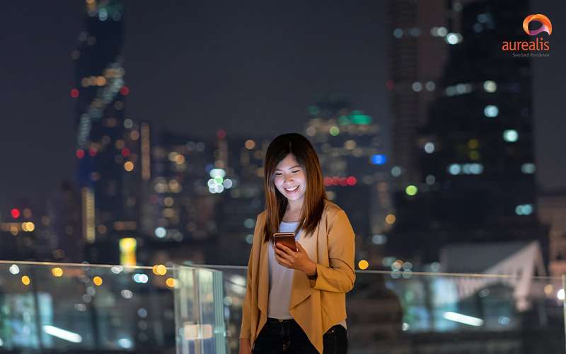 Woman using smartphone on balcony with Singapore skyline view.